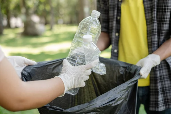 ゴミ収集ボランティアチームはペットボトルを拾いゴミを黒いゴミ袋に入れて公園で清掃し汚染を避け環境や生態系に配慮する — ストック写真