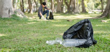 Plastik şişe. Genç Asyalı erkekler plastik şişeleri toplar, parkları temizlemek, kirlilikten kaçınmak, çevreye ve ekosisteme dost olmak için çöpleri siyah çöp torbalarına koyarlar..