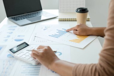 Finans sektöründe çalışan bir kadın evinde oturup yatırımlarının sonuçlarını gösteren mali grafikleri hesaplar ve iş büyümesinin adımlarını planlar..