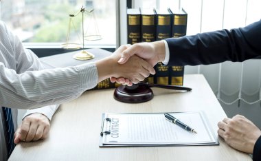 Hukuk bürosunda çalışan profesyonel avukatların tokalaşması için teraziler, adalet terazileri, yargıç tokmağı ve dava belgeleri var. Hukuk ve adalet kavramları.