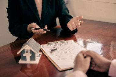 Ev modeli olan bir emlakçı ev kiralamak ve ev sigortası almak için müşterilerle konuşuyor. Ev kiralama ve sigorta konsepti.
