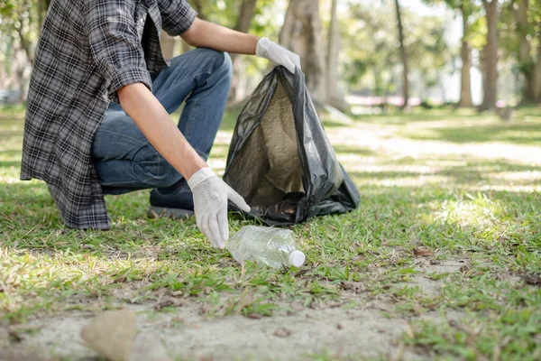 Man's hands pick up plastic bottles, put garbage in black garbage bags to clean up at parks, avoid pollution, be friendly to the environment and ecosystem.