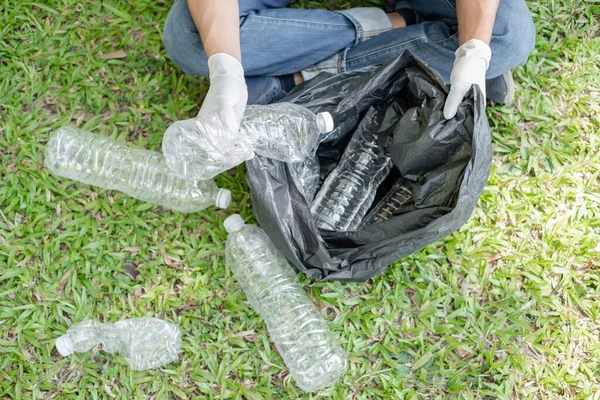 Man\'s hands pick up plastic bottles, put garbage in black garbage bags to clean up at parks, avoid pollution, be friendly to the environment and ecosystem.