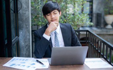 Genç Asyalı iş adamı finansal piyasa analisti masalarında oturuyor ve başarılı iş büyüme sürecini planlayan yatırımlarının sonuçlarını gösteren mali grafikleri hesaplıyor..