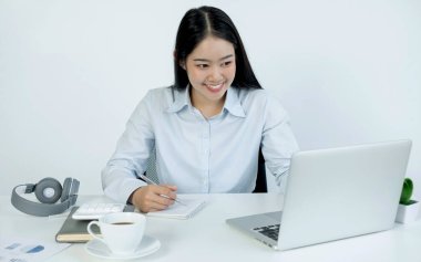 Bilgisayarda çalışan Asyalı kadın. Başarılı gülümseyen iş kadını ofiste çalışıyor ve notlar alıyor..