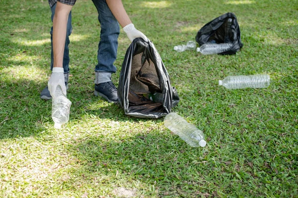 Man\'s hands pick up plastic bottles, put garbage in black garbage bags to clean up at parks, avoid pollution, be friendly to the environment and ecosystem.