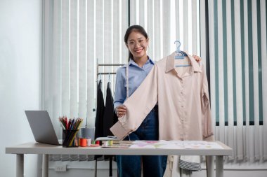 Tekstil aksesuarları ve girişimci tasarımcı çizimleriyle genç ve güzel Asyalı moda terzisi stüdyoda yaratıcı fikirler için dizüstü bilgisayarı olan parlak renklerle dolu..