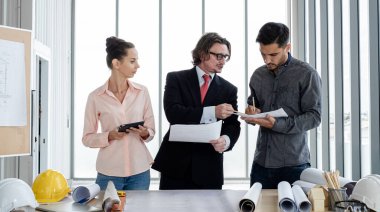 Erkek ve kadın mühendisler ve mimarlardan oluşan bir ekip, çalışma ekibi, inşaat planlarını tartışıyor ve çiziyor, baskı yapıyor, inşaat alanlarında yazıyor..