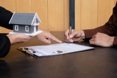 Ev modeli olan bir emlakçı, müşterilerle ev sigortası satın almak ve resmi sözleşme altında müşterilere sözleşme imzalatmak hakkında konuşuyor. Ev kiralama ve sigorta konsepti.