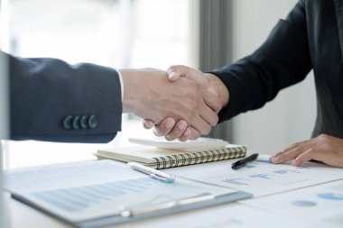 İki iş adamı el sıkışarak grafikler, finansal grafikler hakkında konuşuyor. Sonuçları gösteren planlama stratejileri analiz ediyor ve hesaplıyor. Ticari başarı oluşturma süreçleri..