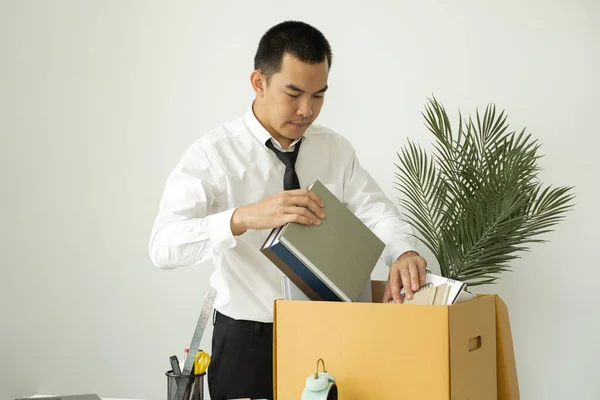 A male office worker is unhappy with being fired from a company packing things into cardboard boxes. The young man was stressed and disappointed by being fired. concept of layoffs and unemployment.