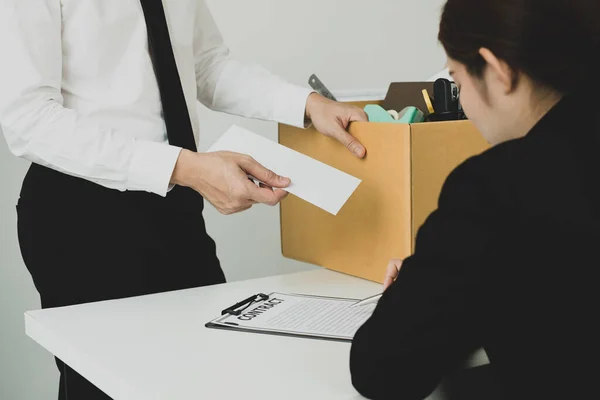 Desperately fired man office worker employee hands her employer her resignation letter and packs her belongings in a cardboard box concept dismissal and unemployment.