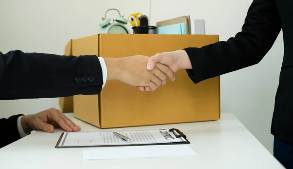 Desperately fired female office worker employee hands her employer her resignation letter, packs her belongings in a cardboard box, and shaking hands with boss concept dismissal and unemployment.