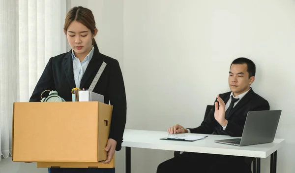 A woman office worker is unhappy with being fired from a company packing things into cardboard boxes. The Young woman was stressed and disappointed by being fired. concept of layoffs and unemployment.