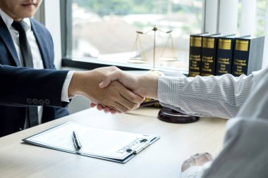 Hukuk bürosunda çalışan profesyonel avukatların tokalaşması için teraziler, adalet terazileri, yargıç tokmağı ve dava belgeleri var. Hukuk ve adalet kavramları.