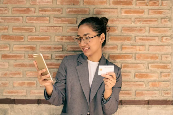 The business Asian woman hand is holding a credit card and uses a smartphone for online shopping and internet payment in a happy way.