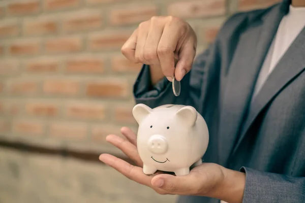 Asian businesswomen hold piggy banks and put coins in piggy banks to save money with coins to step into business, grow successful, and save money. savings concept.
