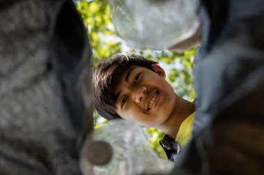 Genç Asyalı erkekler plastik şişeleri toplar, parkları temizlemek, kirlilikten kaçınmak, çevreye ve ekosisteme dost olmak için çöpleri siyah çöp torbalarına koyarlar..