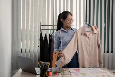 Tekstil aksesuarları ve girişimci tasarımcı çizimleriyle genç ve güzel Asyalı moda terzisi stüdyoda yaratıcı fikirler için dizüstü bilgisayarı olan parlak renklerle dolu..