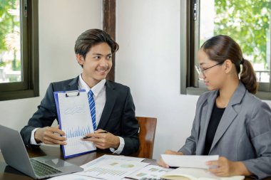 İki iş lideri çizelgeler, finansal grafikler hakkında konuşuyor. Sonuçları gösteren planlama stratejilerini analiz ediyor ve hesaplıyor. Ticari başarı oluşturma süreçlerini de..