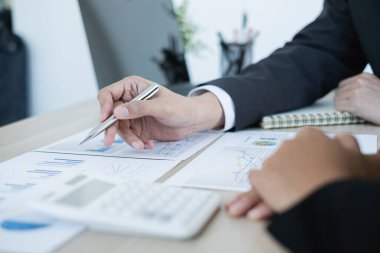 İki iş lideri çizelgeler, finansal grafikler hakkında konuşuyor. Sonuçları gösteren planlama stratejilerini analiz ediyor ve hesaplıyor. Ticari başarı oluşturma süreçlerini de..