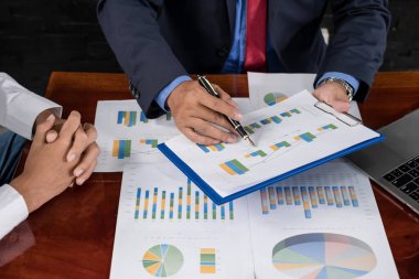 İki iş lideri çizelgeler, finansal grafikler hakkında konuşuyor. Sonuçları gösteren planlama stratejilerini analiz ediyor ve hesaplıyor. Ticari başarı oluşturma süreçlerini de..