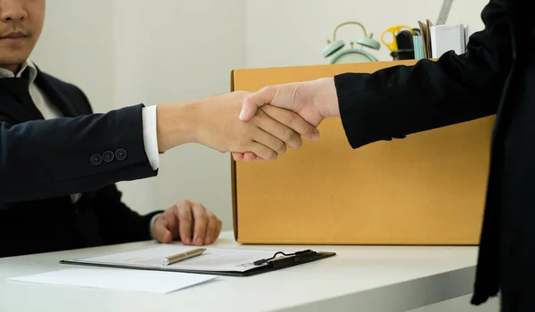 Desperately fired female office worker employee hands her employer her resignation letter, packs her belongings in a cardboard box, and shaking hands with boss concept dismissal and unemployment.