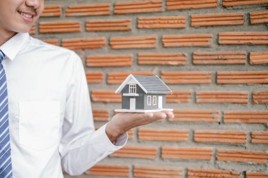 Ev sigortası ve gayrimenkul. Asyalı iş adamı ev modelini elinde tutuyor ev kiralama, ev satın alma ve ev sigortası için yatırım yapıyor..
