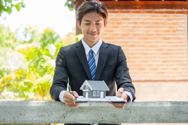 Home insurance concept and real estate. Business Asian man holding a house model working in investment about renting a house, buying a house, and home insurance.