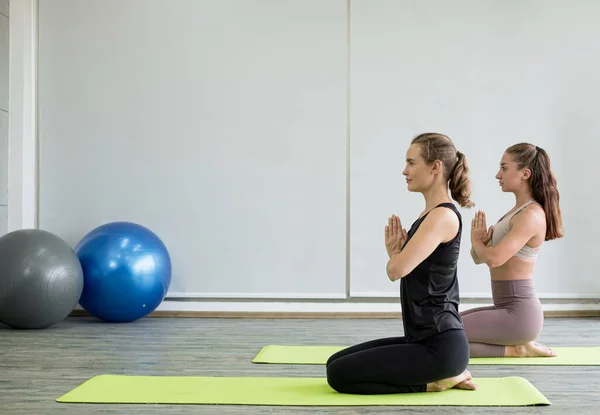Two young women play yoga stretching, exercise for health in fitness, the concept of physical and mental health care.