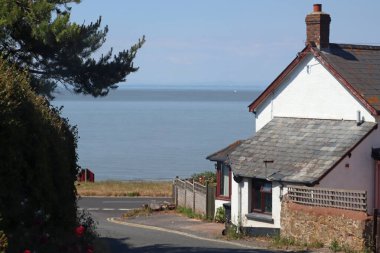 İngiltere, Somerset 'teki Blue Anchor' da denize çok yakın eski bir kulübenin yanından dar bir yol geçiyor.