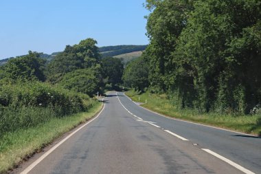 Somerset, İngiltere 'de boş bir yolda yokuş aşağı. Arka planda yemyeşil yuvarlanan tepeler görülebilir