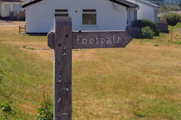 A public footpath sign stands in front of holiday chalet close to a sunny bay at Blue Anchor in Somerset.