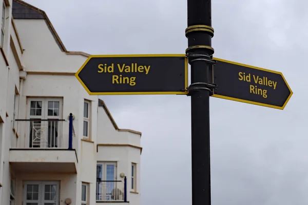 A sign with gold lettering on a black background in Sidmouth, Devon pointing out the route of the Sid Valley Ring walking route. The 13 mile walk was launched in 2019