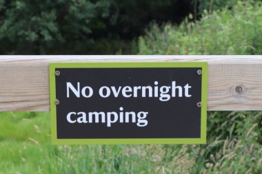 Black and white sign with a green border saying No overnight camping