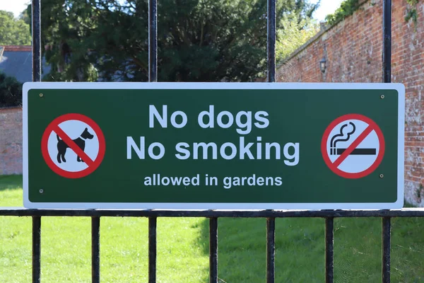 A sign on the metal gate into the grounds of the public garden informing that no Dogs or smoking is allowed