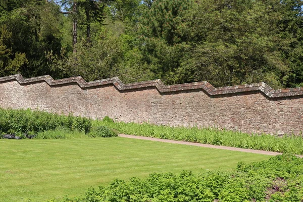 A grassy area in front of the stepped effect of the wall of a kitchen garden at an English stately house near Tiverton in Devon
