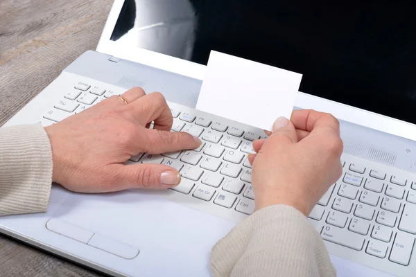 La mujer sostiene una tarjeta y usa la computadora. — Foto de Stock