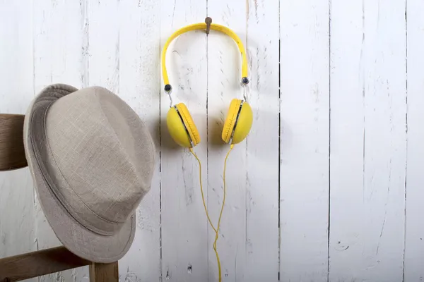 Hat and yellow headphones hung on a wall painting white — Stock Photo, Image