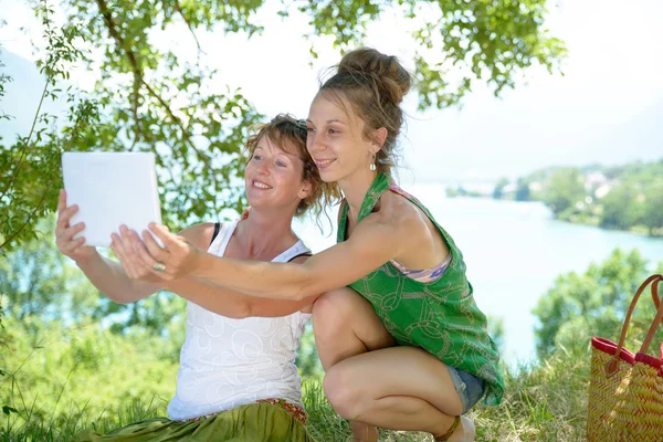 Две симпатичные девушки на траве с цифровым планшетом — стоковое фото