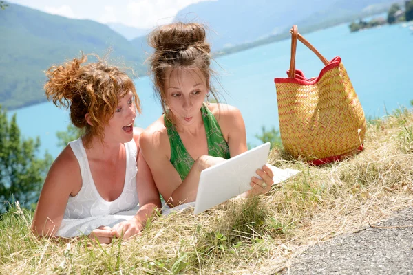 Две симпатичные девушки на траве с цифровым планшетом — стоковое фото
