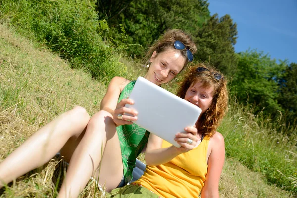 Two pretty girls on the grass with a digital tablet — Stock Photo, Image
