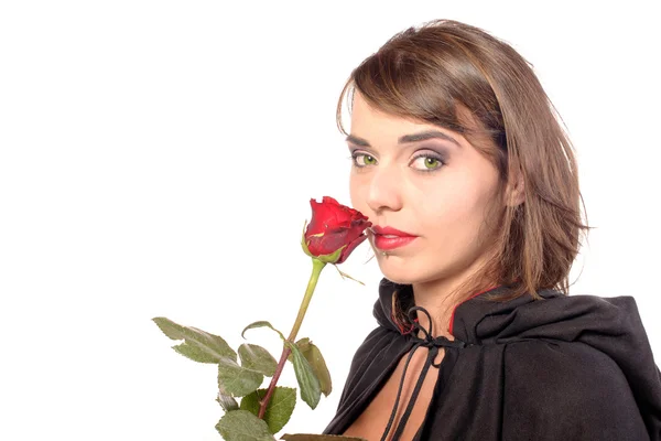 Smiling girl dressed in a black cape smells a red rose — Stock Photo, Image
