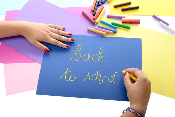 Uma menina escrevendo de volta para a escola em papel azul — Fotografia de Stock