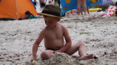 Çocuk kumsalda kumla oynuyor.