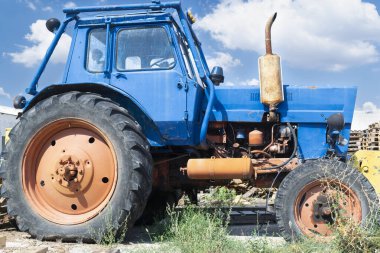 Arka bahçede harap olmuş mavi tekerlekli bir traktör var.