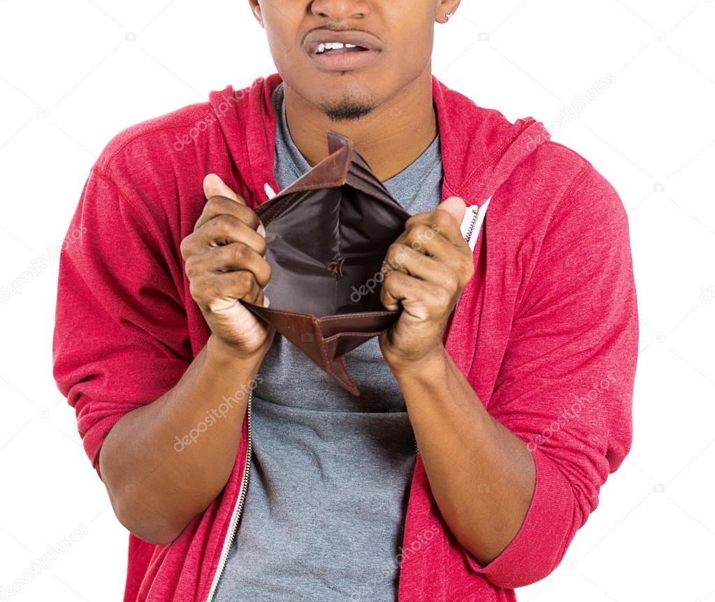 Closeup portrait of stressed, upset, sad, unhappy young man standing with, looking into empty wallet