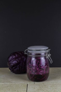 Bir kavanoz taze lahana turşusu, arkasında kırmızı lahana, portre, üstünde koyu bir telif alanı.. 