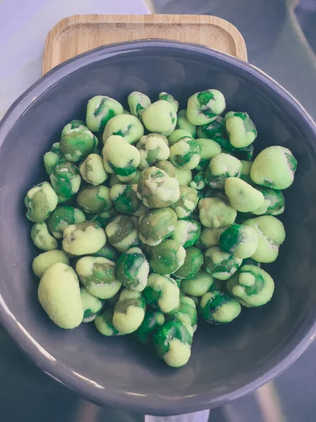 Close up shot of a blue ceramic code filled with wasabi covered peas in a japanese restaurant. Green wasabi on green peas, very spicy starter or appetizer to share. Wooden background.