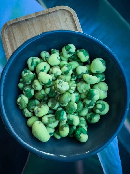 Close up shot of a blue ceramic code filled with wasabi covered peas in a japanese restaurant. Green wasabi on green peas, very spicy starter or appetizer to share. Wooden background.